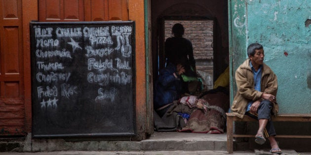 KATHMANDU, NEPAL - APRIL 28: A man sits outside his house while his family pack their belongings inside their damaged house on April 28, 2015 in Kathmandu, Nepal. A major 7.8 earthquake hit Kathmandu mid-day on Saturday, and was followed by multiple aftershocks that triggered avalanches on Mt. Everest that buried mountain climbers in their base camps. Many houses, buildings and temples in the capital were destroyed during the earthquake, leaving thousands dead or trapped under the debris as emergency rescue workers attempt to clear debris and find survivors. Regular aftershocks have hampered recovery missions as locals, officials and aid workers attempt to recover bodies from the rubble. (Photo by Omar Havana/Getty Images)