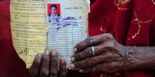 Sita Devi, the mother of Indian farmer Pyare Lal Bind, 45, and who committed suicide after his crops failed, poses for a photograph with an image of her son and the family's ration card Karnipur village, some 35 kms away from Allahabad on April 18, 2015. Unseasonal heavy rains has caused crops to fail across parts of India. AFP PHOTO/ SANJAY KANOJIA (Photo credit should read Sanjay Kanojia/AFP/Getty Images)