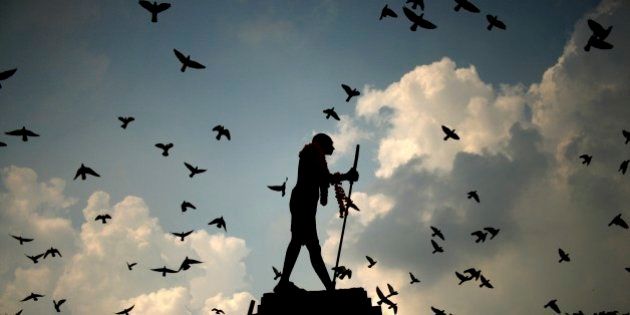 Pigeons fly behind a silhouetted statue of Mahatma Gandhi adorned with garlands on Gandhi's birth anniversary in Amritsar, India Wednesday, Oct. 2, 2013. (AP Photo/Sanjeev Syal)