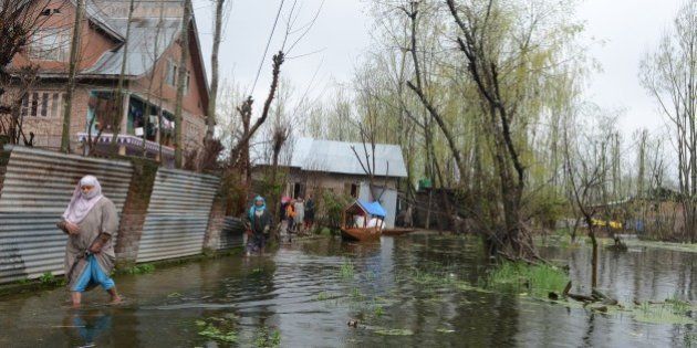 Kashmiri residents walk through floodwaters outside their homes as water levels rise on Dal Lake in Srinagar on April 1, 2015. Many low lying areas in Indian Kashmir were flooded for the second time since September last year. On March 30, fifteen members of two families including a three-week old baby died after they were buried alive by a landslide caused by incessant rains flooding in the region. But officials sounded hope as water levels in River Jhelum, that causes the biggest threat of flooding in Srinagar, continued to decrease. AFP PHOTO/Tauseef MUSTAFA (Photo credit should read TAUSEEF MUSTAFA/AFP/Getty Images)