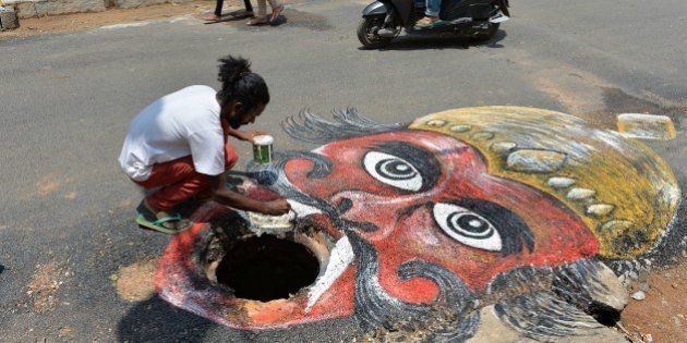 Indian artist Badal Nanjundaswamy uses the opening of an unattended manhole in the middle of a road as a canvas to depict the Hindu God of death 'Yama' waiting to gobble up unwary pedestrains or motorists in Bangalore on June 6, 2014. The art installation was executed to draw the attention of the responsible municipal authorities into fixing the civic problem in an artistic way. AFP PHOTO/Manjunath KIRAN (Photo credit should read Manjunath Kiran/AFP/Getty Images)