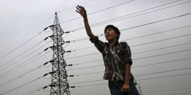 An Indian boy gestures as he stands near high tension electricity tower on a roadside in New Delhi, India, Wednesday, Aug. 1, 2012. Factories and workshops across India were up and running again Wednesday, a day after a major system collapse led to a second day of power outages and the worst blackout in history leaving an estimated 620 million people without electricity. (AP Photo/Kevin Frayer)