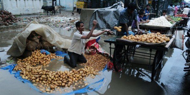 An Indian vegetable vendor removes potatoes from his tarpaulin after heavy monsoon rains inundated a roadside market in Allahabad on August 16, 2015. AFP PHOTO/ SANJAY KANOJIA (Photo credit should read Sanjay Kanojia/AFP/Getty Images)