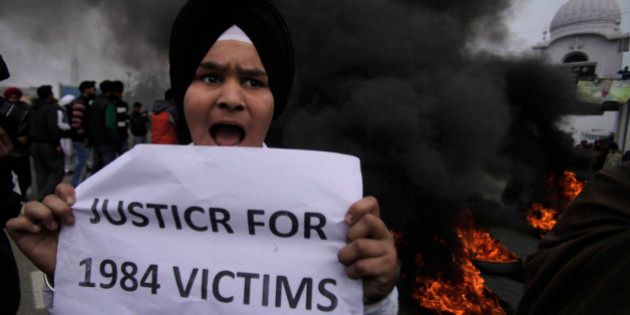 A young Sikh protestor holds a placard as dozens of others burn tires during a protest against Congress party leader Rahul Gandhi for his recent remark on the country's 1984 anti-Sikh riots, in Jammu, India, Sunday, Feb. 2, 2014. Rahul Gandhi in a recent television interview refused to apologize for the riots that killed more than 3,000 Sikhs saying he was not in operation in the Congress party in 1984. Top Congress party leaders have been accused of inciting mobs during the violence that followed the assassination of Prime Minister Indira Gandhi by her Sikh bodyguards. (AP Photo/Channi Anand)