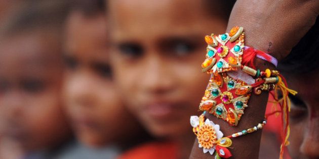 An Indian street child looks at his rakhi tied to his wrist by a member of a voluntary organisation in Kolkata on August 2, 2012. The annual festival of Raksha Bandhan, which commemorates the abiding ties between siblings of opposite sex, is marked by a very simple ceremony in which a woman ties a rakhi, which may be a colourful thread, a simple bracelet, or a decorative string, around the wrist of her brother. AFP PHOTO/Dibyangshu SARKAR (Photo credit should read DIBYANGSHU SARKAR/AFP/GettyImages)