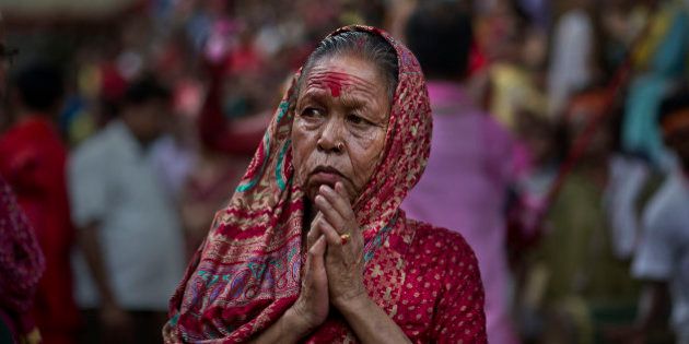 An Indian devotee offers prayers as she watches a priest carry a goat for sacrifice during the Deodhani festival at the Kamakhya Hindu temple in Gauhati, India, Wednesday, Aug. 19, 2015. During this festival devotees sacrifice goats and pigeons. (AP Photo/ Anupam Nath)