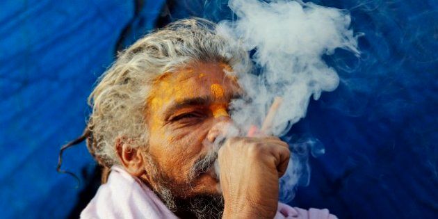 A Sadhu, or Hindu holy man, smokes marijuana to stay warm at Sangam, the confluence of rivers Ganges, Yamuna and mythical Saraswati in Allahabad, India, Sunday, Dec. 21, 2014. Intense cold wave continues unabated in north India with fog disrupting traffic movements at several places. (AP Photo/Rajesh Kumar Singh)