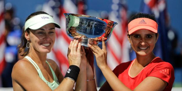 Martina Hingis, of Switzerland, left, and Sania Mirza, of India, hold up the championship trophy after defeating Casey Dellacqua, of Australia, and Yaroslava Shvedova, of Kazakhstan, in the women's doubles championship match of the U.S. Open tennis tournament, Sunday, Sept. 13, 2015, in New York. (AP Photo/David Goldman)