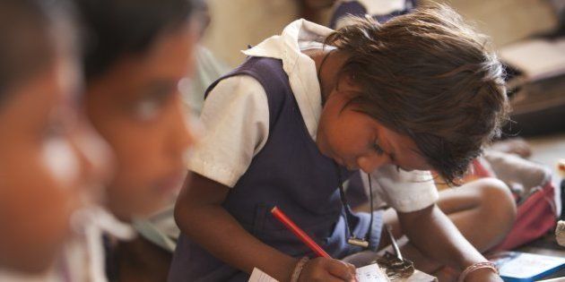 Indian schoolgirl studying in the classroom at her poor village school outside Bandhavgarh National Park. The children sit barefoot on the floor to learn their lessons. She is wearing a school uniform.