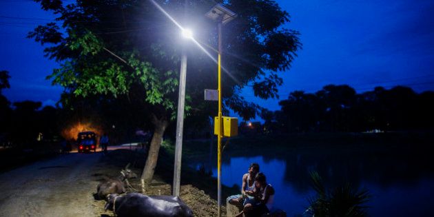 Cows rest by the side of a road as a man and child sit under a light powered by energy from a solar power microgrid at night in the village of Dharnai in Jehanabad, Bihar, India, on Thursday, July 9, 2015. While Prime Minister Narendra Modi's ambition has led billionaires such as Foxconn Technology Group's Terry Gou to pledge investment, the question remains whether the 750 million Indians living on less than $2 per day can afford or will embrace green energy. Photographer: Prashanth Vishwanathan/Bloomberg via Getty Images