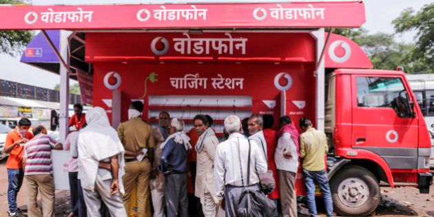 People stand at a Vodafone India Ltd. mobile charging station in Nashik, Maharashtra, India, on Saturday, Sept. 12, 2015. Millions of pilgrims in a landscape awash in saffron make their way to the waters of the holy Godavari River for the Kumbh Mela, the festival of the pitcher. It is one of the largest religious festivals on the face of the planet. Photographer: Dhiraj Singh/Bloomberg via Getty Images