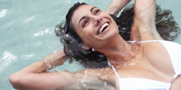Young woman floating in sea, hands behind head, laughing, close-up