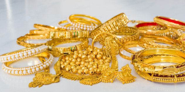 Gold jewellery or jewelry including pure gold bangles and gold with pearl bangles, rings, ear rings, lockets, etc on white marble floor.