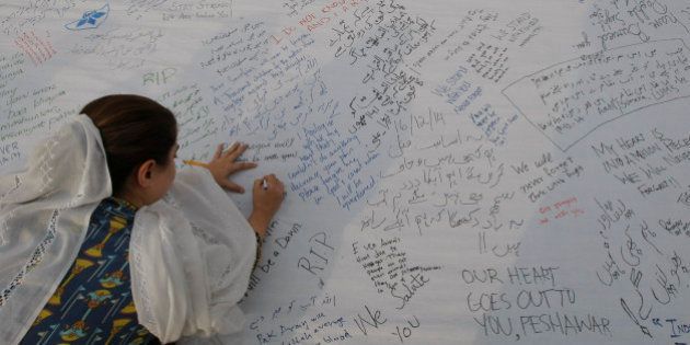 A Pakistani girl writes a message for students killed in a Dec. 16 Taliban attack on a military-run school, in Peshawar, Pakistan, Wednesday, Dec. 24, 2014. The school massacre last Tuesday horrified Pakistanis across the country. The militants, wearing suicide vests, climbed over the fence into a military-run school, burst into an auditorium filled with students and opened fire. The bloodshed went on for several hours until security forces finally were able to kill the attackers. (AP Photo/Muhammad Sajjad)