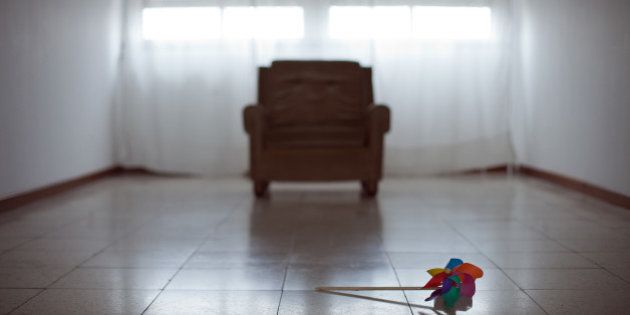 Toy windmill lying on floor of an empty room with sofa and two windows on background.