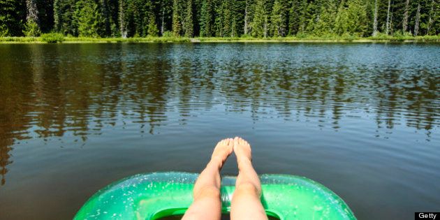 Trees reflecting on beautiful Forlorn Lake in Washington State's Gifford Pinchot National Forest near Mount Adams. Relaxed feet dangle off the edge of a water craft.