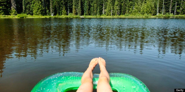 Trees reflecting on beautiful Forlorn Lake in Washington State's Gifford Pinchot National Forest near Mount Adams. Relaxed feet dangle off the edge of a water craft.