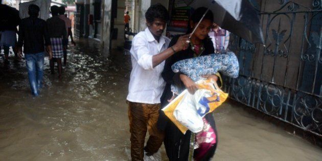 An Indian couple shelter under an umbrella as they walk with their child through floodwaters inundating Egmore Hospital in Chennai on December 1, 2015, during a downpour of heavy rain in the southern Indian city. Heavy rains pounded several parts of the southern Indian state of Tamil Nadu and inundating most areas of Chennai, severely disrupting flights, train and bus services and forcing the postponment of half-yearly school exams. AFP PHOTO/STR / AFP / STRDEL (Photo credit should read STRDEL/AFP/Getty Images)
