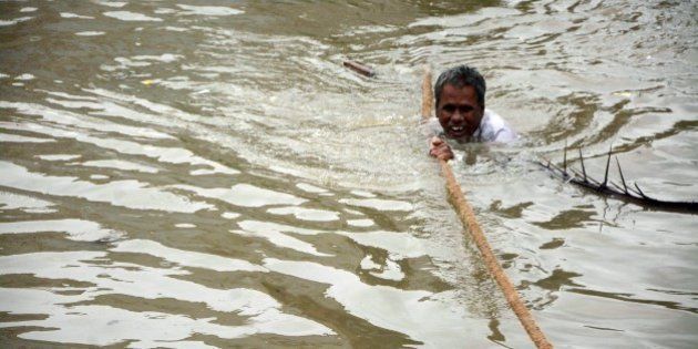 TOPSHOT - An Indian man clings to a rope as he makes his way through floodwaters in Chennai on December 2, 2015. India has deployed troops to Tamil Nadu and closed the main airport there after heavy rains worsened weeks of flooding that has killed nearly 200 people in the southern coastal state. Thousands of rescuers carrying diving equipment, inflatable boats and medical equipment were battling to evacuate victims across the flooded state, officials said. AFP PHOTO/STR / AFP / STRDEL (Photo credit should read STRDEL/AFP/Getty Images)