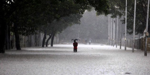 TOPSHOT - An Indian man shelters under an umbrella as he walks through floodwaters in Chennai on December 1, 2015, during a downpour of heavy rain in the southern Indian city. Heavy rains pounded several parts of the southern Indian state of Tamil Nadu and inundating most areas of Chennai, severely disrupting flights, train and bus services and forcing the postponment of half-yearly school exams. AFP PHOTO/STR / AFP / STRDEL (Photo credit should read STRDEL/AFP/Getty Images)