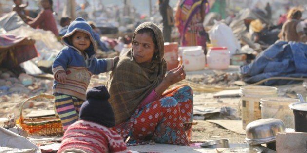 NEW DELHI, INDIA - DECEMBER 13: Stranded people sit near their demolished shanties after more than 500 slums were demolished last night in an anti-encroachment drive conducted by the Indian Railways at Shakur Basti, on December 13, 2015 in New Delhi, India. Slum residents created uproar after a child was found dead. They alleged that the child had died in the anti-encroachment drive. Railway denied the allegations, saying that the death of the child occurred in one of the slums and had nothing to do with the removal of encroachments. (Photo by Arvind Yadav/Hindustan Times via Getty Images)