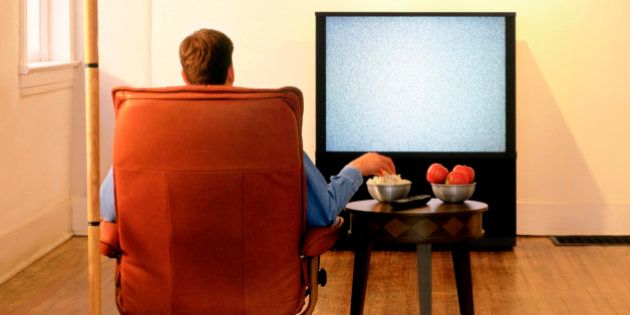 Rear view of a man sitting in an armchair and watching television