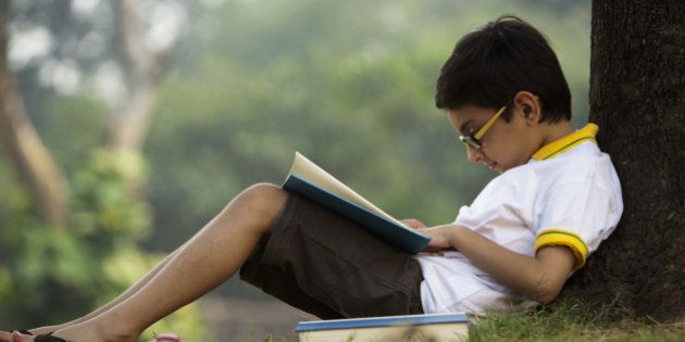Boy (6-7)reading books under tree in park