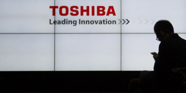 A man sits using a smartphone in front of the Toshiba Corp. logo displayed on screens in Tokyo, Japan, on Monday, Dec. 21, 2015. Toshiba forecast a record 550 billion yen ($4.5 billion) loss and will cut more jobs and restructure businesses that include chips, televisions, personal computers and home appliances following a long-running accounting scandal. Photographer: Tomohiro Ohsumi/Bloomberg via Getty Images