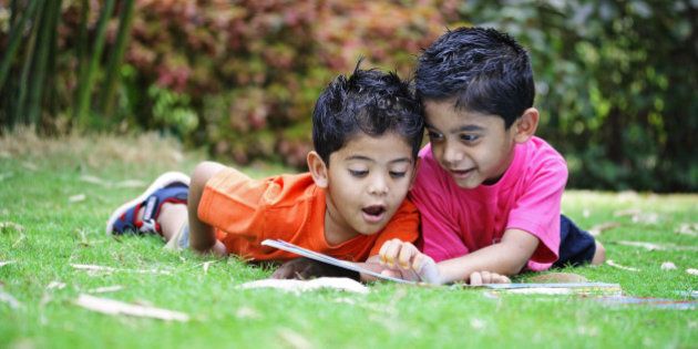 Two kids reading a book, in a park