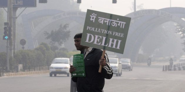 NOIDA, INDIA - JANUARY 1: A Civil Defence personnel holds a placard as he stands at a traffic intersection on the first day of Delhi's Odd-Even Vehicle Plan, on January 1, 2016 in Noida, India. The odd-even scheme that allows odd and even-numbered private vehicles to ply on city roads on alternate days aims at reducing air pollution levels. All diesel and petrol cars, irrespective of where they are coming from, will have to follow the rules. If a car is coming from out of Delhi and is breaking the odd-even rule, a fine will be levied. The government has deployed hundreds of volunteers and 3000 buses to help traffic police. To clean the Capitalâs toxic air, only odd-numbered private cars will be allowed on the road on odd dates and even-numbered on even days. Violators face a fine of Rs. 2,000. More than a million private cars were banned from New Delhi's roads as authorities began trialling drastic new measures to cut smog in the world's most polluted capital. (Photo by Burhaan Kinu/Hindustan Times via Getty Images)