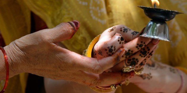 An elderly lady holds the henna-decorated hands of a married Hindu woman as they offer prayers with an oil lamp on the occasion of 'Vata Savitri Poornima' in Mumbai on June 12, 2014. On the occasion of Vata Savitri Purnima married Hindu women keep a fast for the long-life and good health of their husbands and break their fast by performing rituals beneath a banyan tree. The day's ritual involves worshipping a banyan (vata) tree by applying holy 'red kumkum' (vermillion) and turmeric and placing flowers and lighting incense sticks reverentially and culminates with the women circumambulating the tree seven times round, unwinding a spool of white thread in their hands as a priest recites mantras. AFP PHOTO/ INDRANIL MUKHERJEE (Photo credit should read INDRANIL MUKHERJEE/AFP/Getty Images)