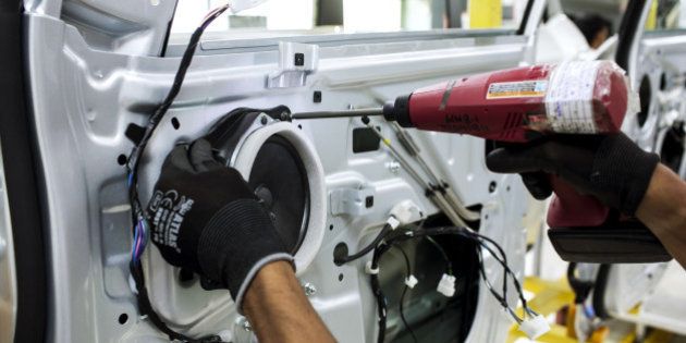 An employee uses a drill to fit a speaker to the door of a Mahindra & Mahindra Ltd. XUV 500 sport-utility vehicle (SUV) on the production line at the company's facility in Chakan, Maharashtra, India, on Wednesday, Sept. 12, 2014. Mahindra, Indias largest maker of tractors and sport-utility vehicles, is in advanced talks to buy PSA Peugeot Citroens scooter business, according to three people familiar with the matter. Photographer: Udit Kulshrestha/Bloomberg via Getty Images