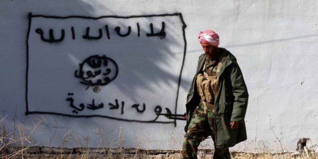 A Kurdish fighter walks by a wall bearing a drawing of the flag of the Islamic State (IS) group in the northern Iraqi town of Sinjar, in the Nineveh Province, on November 13, 2015. Iraqi Kurdish leader Massud Barzani announced the 'liberation' of Sinjar from the Islamic State group in an assault backed by US-led strikes that cut a key jihadist supply line with Syria. AFP PHOTO / SAFIN HAMED / AFP / SAFIN HAMED (Photo credit should read SAFIN HAMED/AFP/Getty Images)