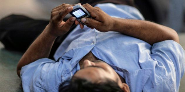 A man uses a mobile phone as he reclines in Mumbai, India, on Monday, Oct. 19, 2015. Telecom operators were allowed to trade wireless airwaves with rivals in September by the government if they were acquired through an auction since 2010 or the holder paid market value initially. Photographer: Dhiraj Singh/Bloomberg via Getty Images