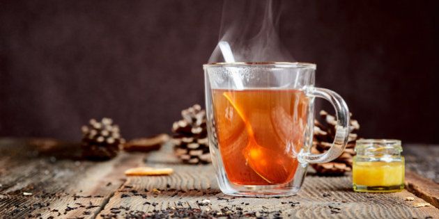 Hot black tea with steam and a little honey pot on a wooden table
