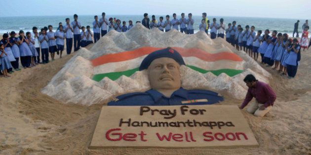 Indian students stand and pray near a sand sculpture created by Sudarsan Pattnaik of Hanumanthappa Koppad, rescued alive five days after being buried in an avalanche in the Himalayas, at Puri beach, some 65 km from Bhubaneswar, on February 10, 2016. An Indian soldier's condition deteriorated February 10, two days after his dramatic rescue from under mounds of snow nearly a week after being buried alive in an avalanche, the army said. AFP PHOTO/ASIT KUMAR / AFP / ASIT KUMAR (Photo credit should read ASIT KUMAR/AFP/Getty Images)