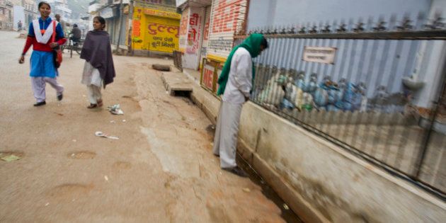 Varanasi, India. An Indian man urinates in the street while two girls walk behind him.