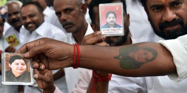 Supporters of India's former southern Tamil Nadu state chief minister J. Jayalalithaa display her photographs and an arm tattooed with her portrait as they wait outside the Bangalore Central Jail for her release on bail in Bangalore on October 18, 2014. India's top court granted bail October 17 to a powerful south Indian film star-turned-politician jailed last month for corruption, a ruling that sparked jubilation in her home state. Jayalalithaa Jayaram, 66, an ex-film star and a longtime head of Tamil Nadu, was convicted last month of having land, gold and other assets vastly exceeding her income in a case that had dragged on for nearly two decades, and sentenced to four years in jail. AFP PHOTO/Manjunath KIRAN (Photo credit should read MANJUNATH KIRAN/AFP/Getty Images)