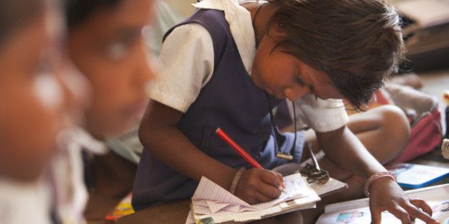 Indian schoolgirl studying in the classroom at her poor village school outside Bandhavgarh National Park. The children sit barefoot on the floor to learn their lessons. She is wearing a school uniform.