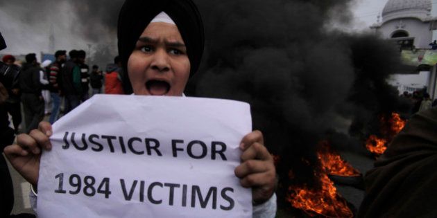 A young Sikh protestor holds a placard as dozens of others burn tires during a protest against Congress party leader Rahul Gandhi for his recent remark on the country's 1984 anti-Sikh riots, in Jammu, India, Sunday, Feb. 2, 2014. Rahul Gandhi in a recent television interview refused to apologize for the riots that killed more than 3,000 Sikhs saying he was not in operation in the Congress party in 1984. Top Congress party leaders have been accused of inciting mobs during the violence that followed the assassination of Prime Minister Indira Gandhi by her Sikh bodyguards. (AP Photo/Channi Anand)