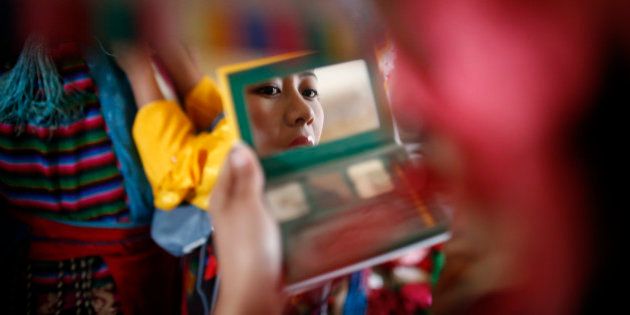 A Tibetan girl in traditional attire looks into the mirror as she prepares ahead of a performance during a function organised to mark
