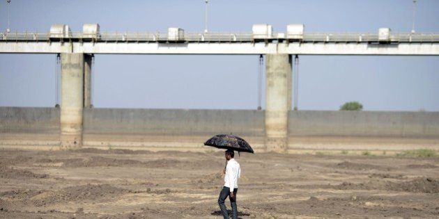 An Indian man holds an umbrella as he walks on the dry reservoir bed next to Gunda Dam by Gunda village in Botad district, some 150 km from Ahmedabad in India's western Gujarat state, on April 1, 2016. Vast regions of western India have been facing acute water shortages due to drought conditions. / AFP / SAM PANTHAKY (Photo credit should read SAM PANTHAKY/AFP/Getty Images)