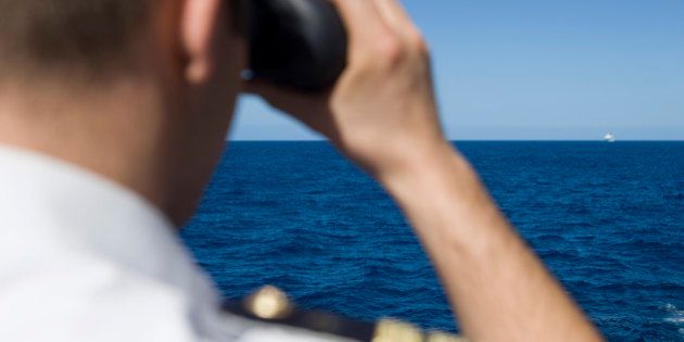 Officer looks through binoculars with cruise ship in distance, near Mozambique, Indian Ocean.