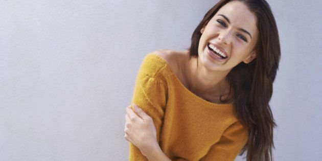 Portrait of a beautiful young woman laughing while standing against a gray wall
