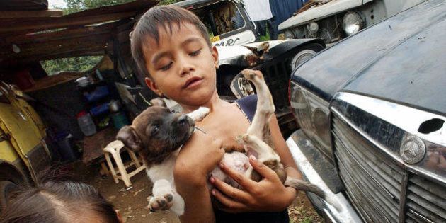 Two Filipino squatter children Jumel Alonte and her younger sister Angel (L) play with their puppy in a junkyard along a highway near the House of Representatives in suburban Quezon City 03 July 2003. The junkyard of abandoned vehicles has been home to at least eight squatter families. The roadside junkyard will be removed on July 05 to give way for a road widening project of the Metro-Manila Developmnent Authority (MMDA). AFP PHOTO/Romeo GACAD (Photo credit should read ROMEO GACAD/AFP/Getty Images)