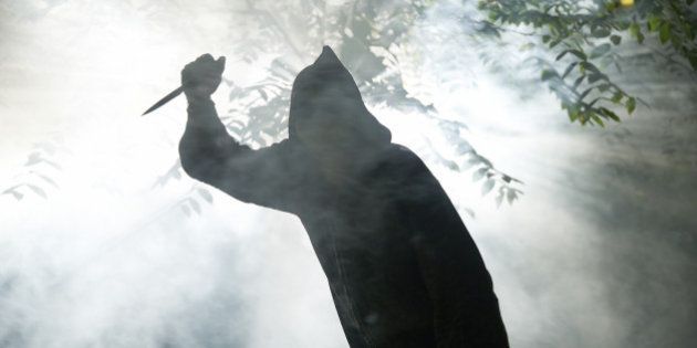 hooded monster with knife in forest coming towards camera light and fog around