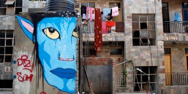 A woman looks out from the balcony of her house, as a street-art resembling a character from the Hollywood film 'Avatar' is seen on a wall in New Delhi, India, Saturday, March 31, 2012. Artists from diverse backgrounds have contributed in the street art festival aimed at building a creative movement in the New Delhi neighborhood. (AP Photo/Tsering Topgyal)