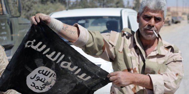 A Syrian soldier displays on April 4, 2016 an Islamic State (IS) group flag after Syrian troops regained control the previous day of al-Qaryatain, a town in the province of Homs in central Syria.IS jihadists withdrew from the town a week after the Russian-backed army and allied militia scored a major victory in the ancient city of Palmyra, which is also located in the vast province of Homs. The recapture of al-Qaryatain allows the army to secure its grip over Palmyra, where jihadists destroyed ancient temples during their 10-month rule and executed 280 people. / AFP / JOSEPH EID (Photo credit should read JOSEPH EID/AFP/Getty Images)