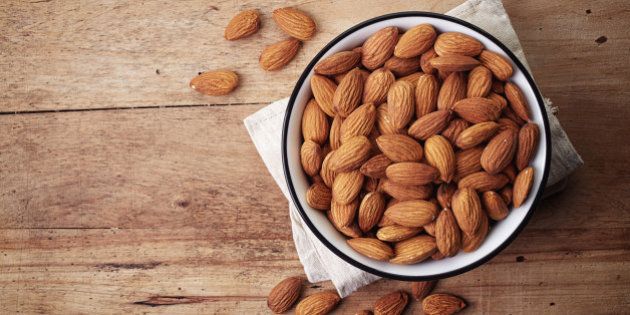 White bowl of almonds on wooden background