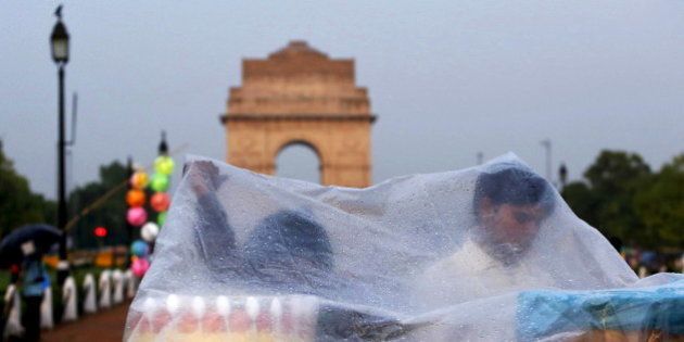 Roadside eatery hawkers use a plastic sheet to cover themselves from a rain shower in front of India Gate in New Delhi, India, June 23, 2015. Officials at the India Meteorological Department (IMD) say the northern states will receive heavier monsoon rains this week but that current weather patterns still point to total rains of just 88 percent of the long-term average, as predicted in early June, due to an El Nino weather pattern. REUTERS/Anindito Mukherjee